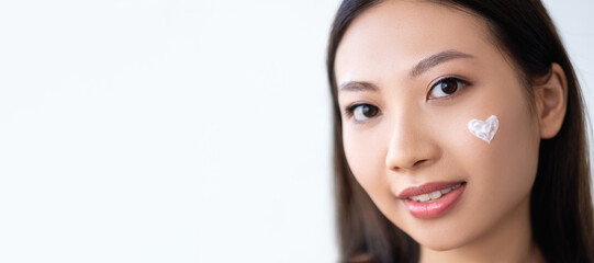 Facial care. Skin moisturizing. Korean cosmetics. Portrait of Asian woman with natural makeup heart shape lotion on perfect smooth face isolated on white empty space background.