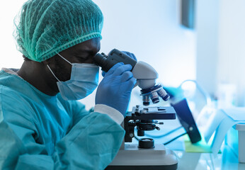 scientist working in laboratory examining coronavirus through microscope - science and technology co