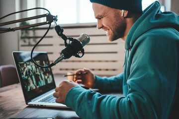 Wall Mural - Handsome smiling host streaming his live podcast using microphone and laptop at his homemade broadcast studio