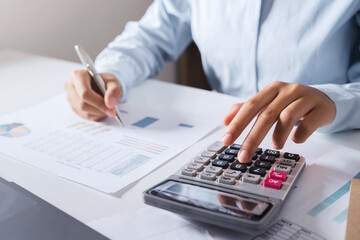 Poster - Woman accountant use calculator and computer with holding pen on desk in office. finance and accounting concept