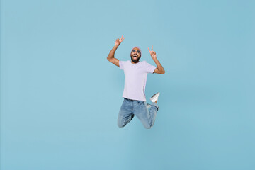 Sticker - Full length young happy cool excited overjoyed unshaven black african man wearing violet t-shirt hat glasses show victory v-sign gesture jump high isolated on pastel blue background studio portrait.