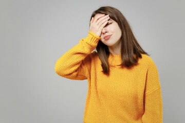 Young excited happy cute indignant confused caucasian woman 20s wearing casual knitted yellow sweater put hand on face facepalm epic fail gesture isolated on grey color background studio portrait.