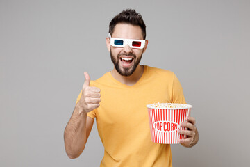 Poster - Young man in 3d glasses yellow t-shirt watch movie film, holding bucket of popcorn show thumb up like gesture isolated on grey background studio. People sincere emotions in cinema, lifestyle concept.