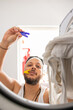 © Erik González - Young man with unkempt appearance prepares his clothes to be washed in the washing machine