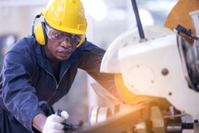 Black Male African American Workers Wear Sound Proof Headphones And Yellow Helmet Working An Iron Cutting Machine In Background Factory Industrial.