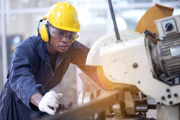 Black male african american workers wear sound proof headphones and yellow helmet working an iron cutting machine in background factory Industrial.