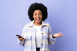© luismolinero - Young African American woman using mobile phone isolated on purple background with shocked facial expression