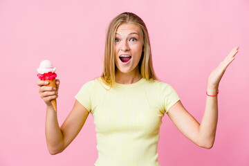 Wall Mural - Young russian woman eating an ice cream isolated receiving a pleasant surprise, excited and raising hands.