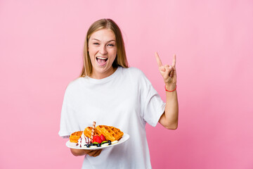 Wall Mural - Young russian woman eating a waffle isolated showing a horns gesture as a revolution concept.