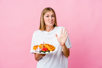 Wall Mural - Young russian woman eating a waffle isolated rejecting someone showing a gesture of disgust.