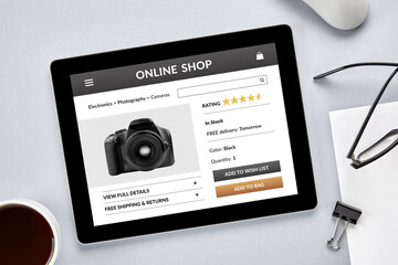 Online shopping of digital camera concept. Tablet computer with online shop app on screen over gray desk. Top view.