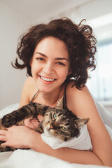 Wall Mural - Gorgeous brunette curly woman relaxing on bed with her striped cat