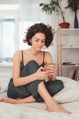 Wall Mural - Young woman staring at her smartphone screen in bed at the morning