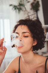 Wall Mural - Woman sitting at her modern bedroom and smoking marijuana hand-rolled cigarettes