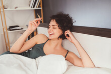 Pleased Girl Laying At The Bed And Enjoying Her Lazy Day At Home At The Morning With Cannabis Cigarette. Funny Mood And Marijuana Concept. Stock Photo