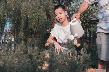 Asian special child on wheelchair watering the plants, Development activities and relationships with family time in the house,Lifestyle in education age and happy disabled kid concept.