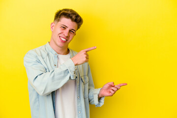 Young caucasian man isolated on yellow background pointing with forefingers to a copy space, expressing excitement and desire.