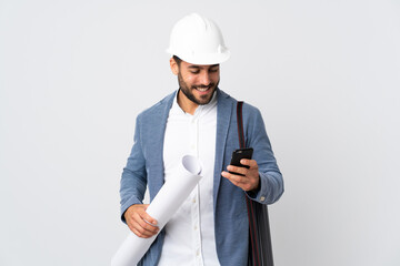 Wall Mural - Young architect man with helmet and holding blueprints isolated on white background sending a message with the mobile