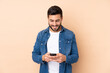 © luismolinero - Caucasian handsome man isolated on beige background sending a message with the mobile