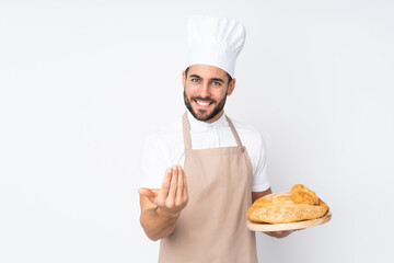 Male baker holding a table with several breads isolated on white background inviting to come