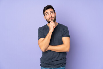 Caucasian handsome man and looking up over isolated purple background