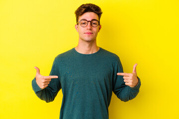 Wall Mural - Young caucasian man isolated on yellow background person pointing by hand to a shirt copy space, proud and confident