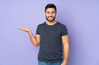 © luismolinero - Caucasian handsome man holding copyspace imaginary on the palm to insert an ad over isolated purple background