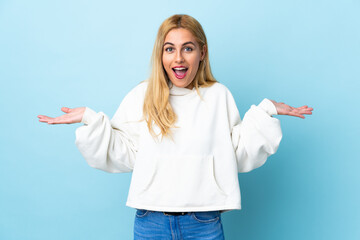 Young Uruguayan blonde woman over isolated blue background with shocked facial expression