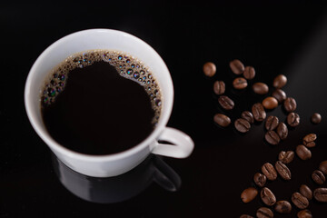 Poster - High angle shot of a cup of fresh coffee and roasted coffee beans on a black background