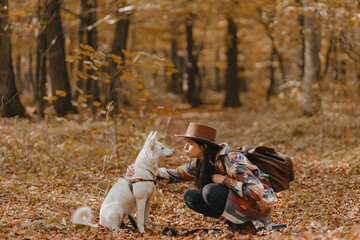 Stylish woman caressing adorable white dog in sunny autumn woods. Cute swiss shepherd puppy