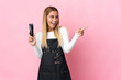 Young hairdresser woman isolated on pink background pointing finger to the side and presenting a product