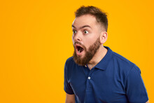 Shocked young man looking away with astonishment in yellow studio