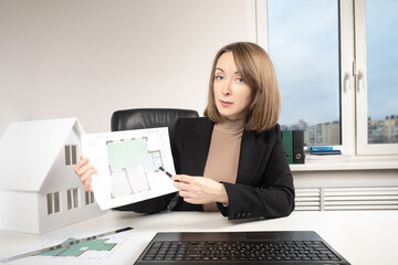 Poster - A woman shows a drawing of a cottage to the camera. An architect presents a construction project online. Remote sale of real estate. Remote consultation of buyers of private houses.