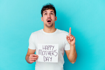 Wall Mural - Young caucasian man holding a happy mothers day placard isolated pointing upside with opened mouth.
