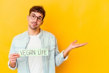 Wall Mural - Young caucasian man holding a vegan life placard isolated showing a copy space on a palm and holding another hand on waist.