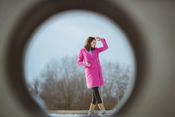 Poster - Attractive brunette female in a pink coat posing for the camera, shot through a hole