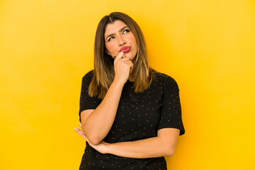 Wall Mural - Young indian woman isolated on yellow background relaxed thinking about something looking at a copy space.