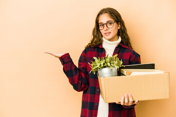 Wall Mural - Young caucasian woman moving holding a box isolated showing a copy space on a palm and holding another hand on waist.