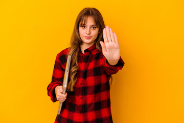 Young caucasian woman holding a laptop isolated standing with outstretched hand showing stop sign, preventing you.