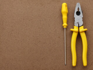 Hand tools for home use (pliers and screwdriver) on a plywood texture