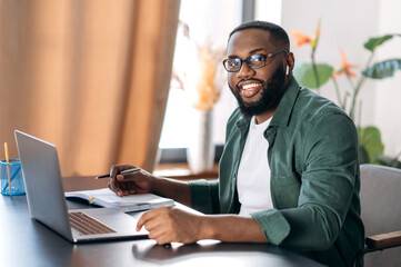 attractive friendly african american guy, successful freelancer, manager or student, sits at his des