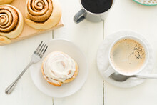 Top View Of A Cinnamon Roll With Frosting With A Coffee Cup