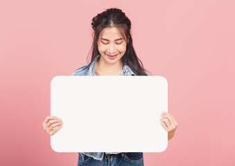 Happy Asian beautiful young woman smiling excited wear denims holding empty speech bubble sign, Portrait female posing show up for your idea looking at bubble, studio shot isolated on pink background