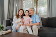 © tirachard - Asian grandparents watch TV with granddaughter at home. Senior Chinese, grandfather and grandmother happy using family time relax with young girl kid lying on sofa in living room concept.