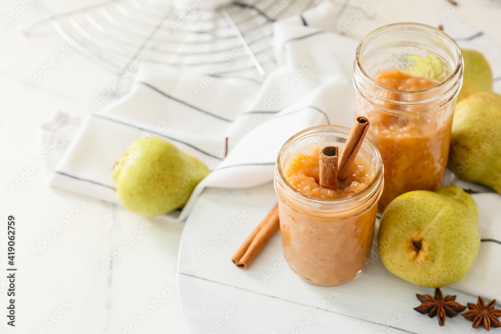 Jars of tasty pear jam on white background