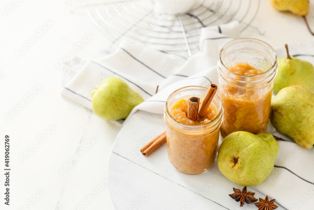 Jars of tasty pear jam on white background