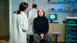 © DC Studio - Doctor specialist in neurological medicine typing health informations of patient. Woman wearing eeg headset answering to medical researcher, monitor showing brain scan in equipped laboratory