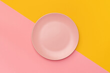 Pink plate on a background divided diagonally into pink and yellow. Minimalism. Minimal cooking concept