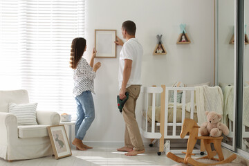 Poster - Happy couple decorating baby room with pictures together. Interior design