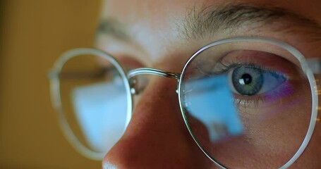 Close up macro shot of reflection in glasses. Young woman with beautiful blue eyes look at screen of laptop or desktop computer. Processing of big data and internet information